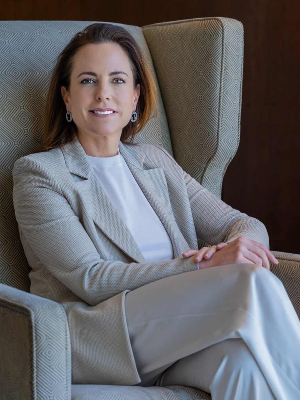 Adriana Cisneros, seated in a wingback chair, smiles to camera