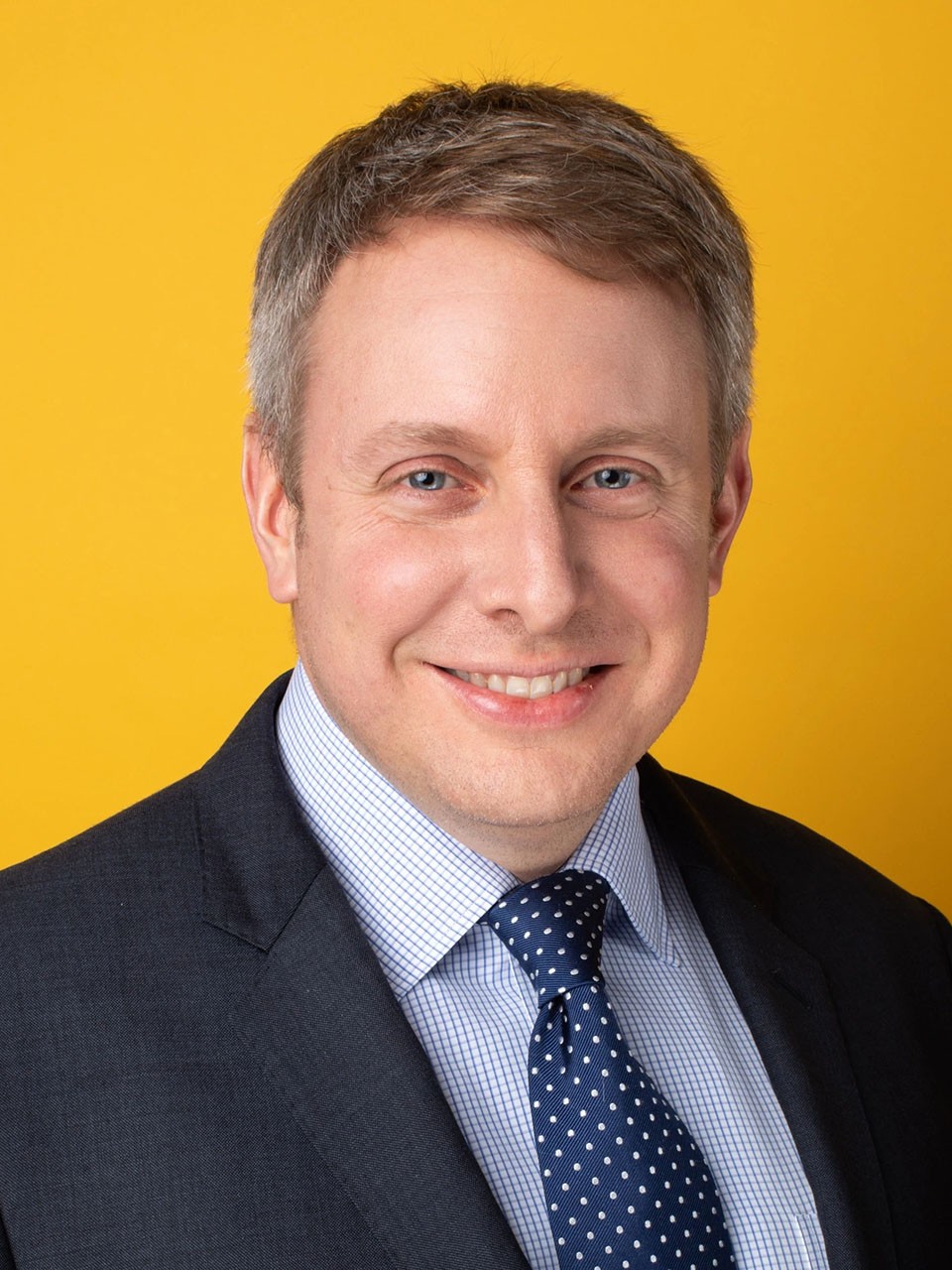 Henry Ford III, in a studio with a marigold wall, smiles to camera