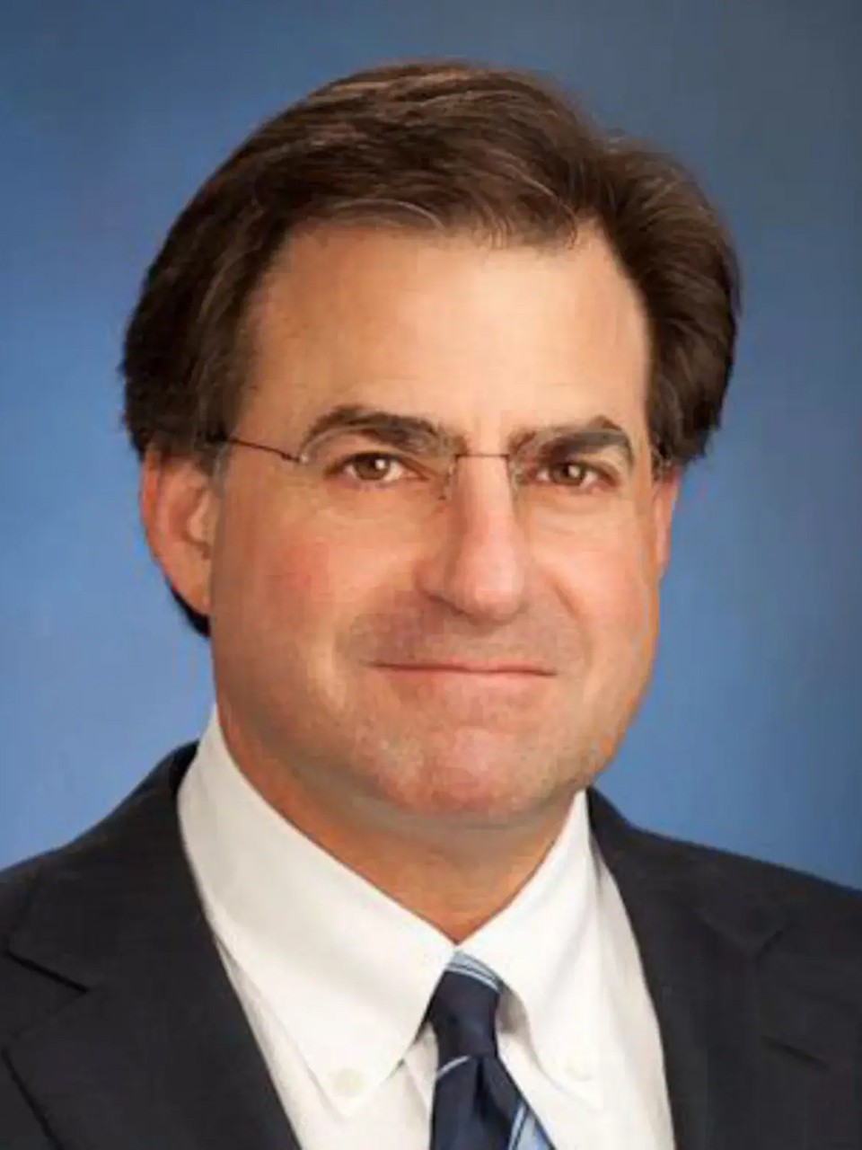John Weinberg, in a studio with blue background, smiles to camera