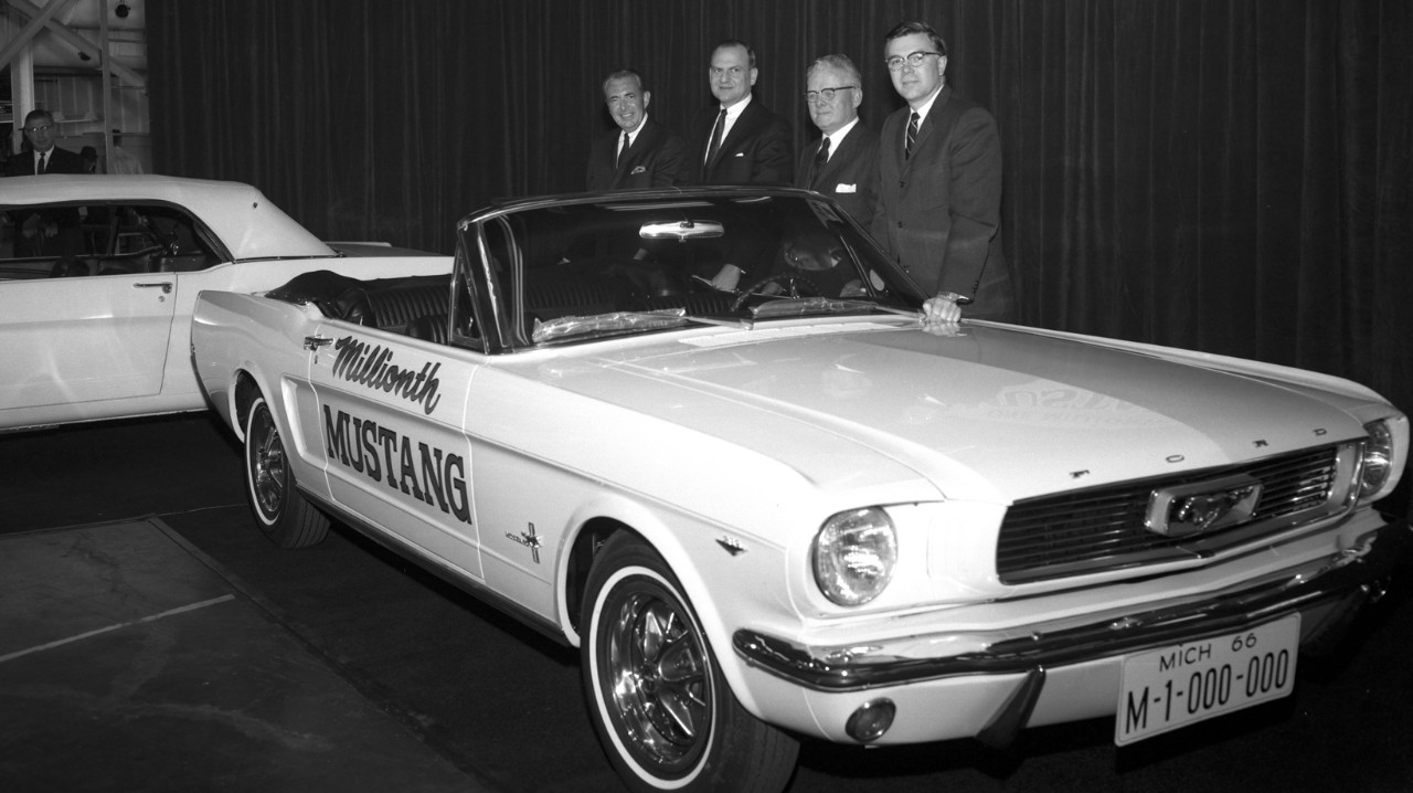 Three men posing in front of a Mustang car 