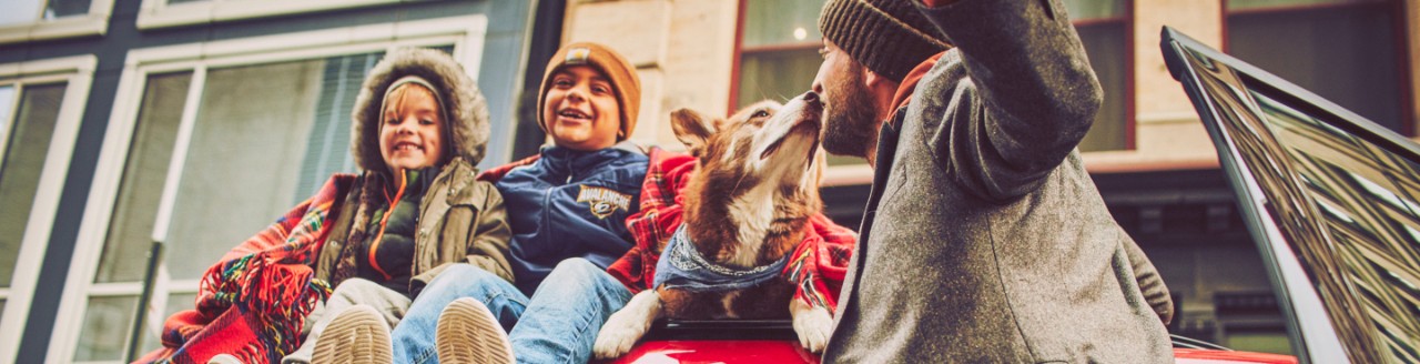 Two kids with a dog and a man smiling and sitting on a red Ford vehicle