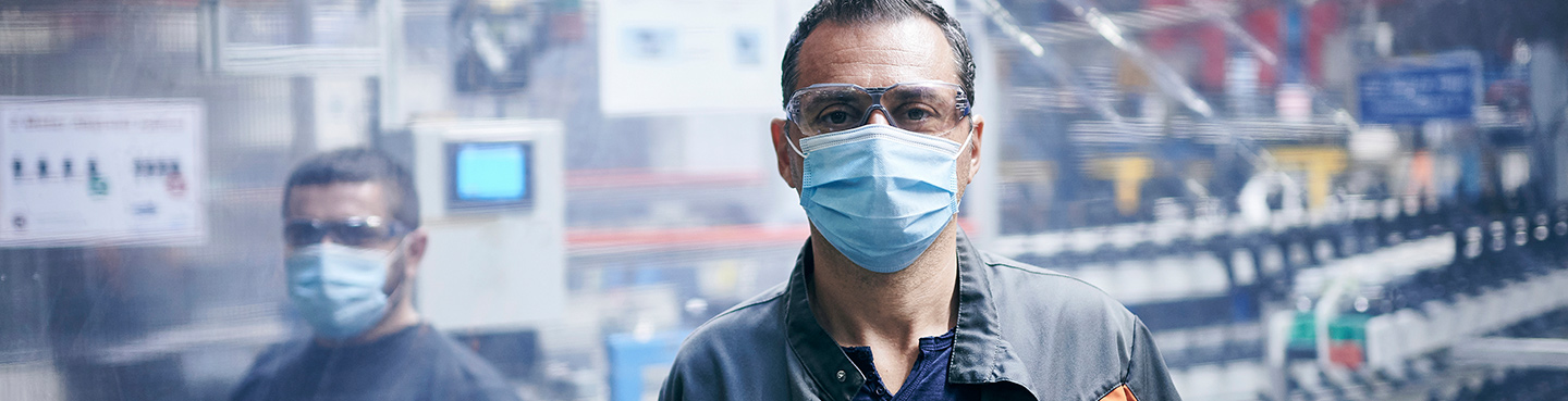 two men wearing face masks with machinery in shop