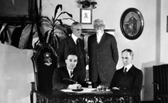 A black and white image of three men standing around a desk