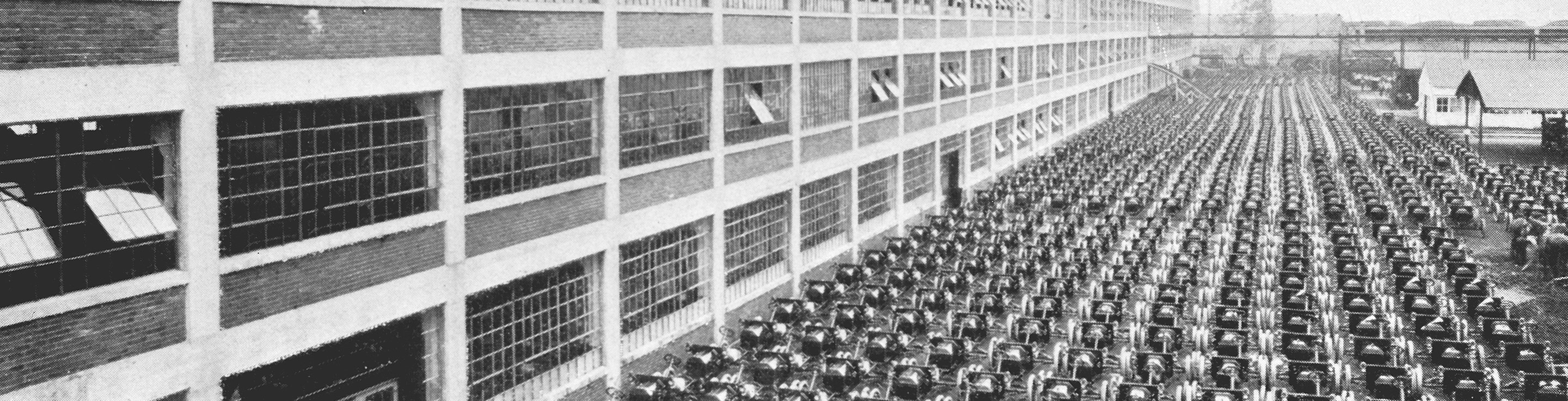 A black and white photo of hundreds of automobiles lined up in front of a Ford plant