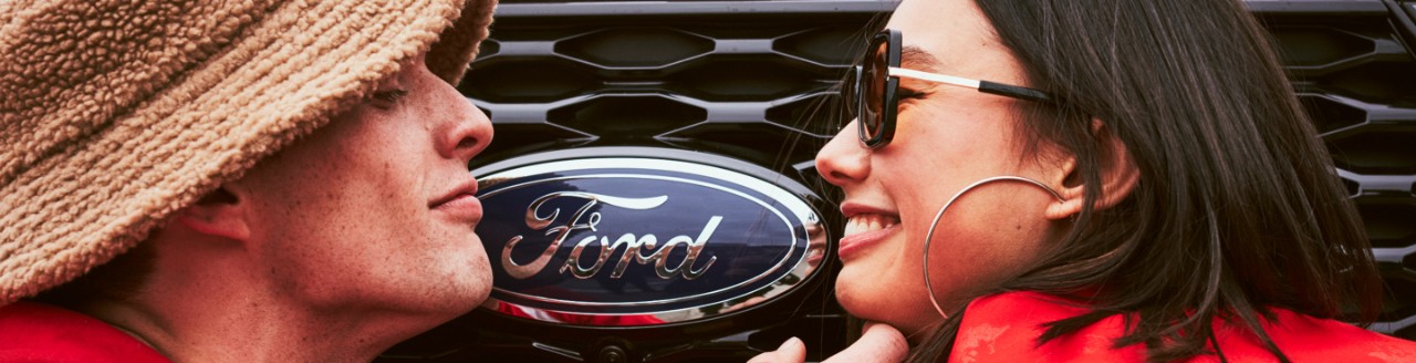 A man and woman smiling at each other in front of a Ford vehicle