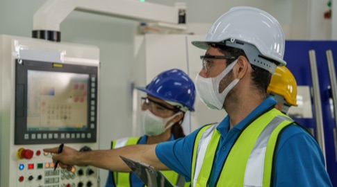 Technicians wearing face mask, safety vest and helmet in control room