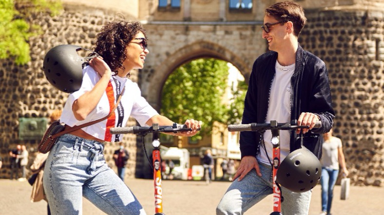 Two friends standing and talking together on the street with their SPIN scooters
