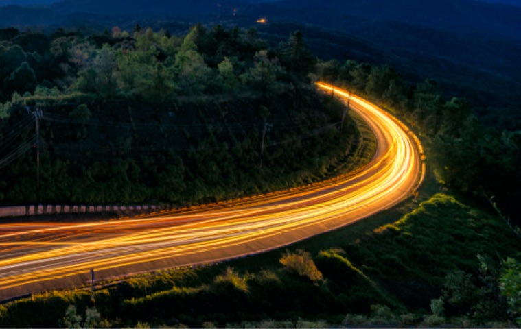Aerial view of a road with vehicle light trails passing through woodland