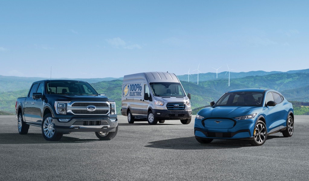 Three of Ford's portfolio of electric vehicles with green mountains and wind turbines in the distance